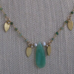 May include: A gold necklace with a green gemstone pendant and small gold leaf charms. The necklace is made with green and white beads.