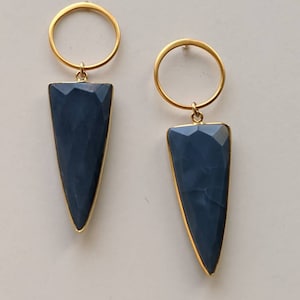 May include: A pair of gold hoop earrings with a dark blue, triangular shaped gemstone pendant.