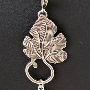 May include: A silver necklace with a pendant featuring a detailed leaf design and a teardrop-shaped stone with black and white patterns.