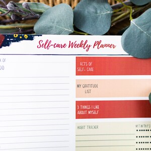 May include: A white self-care weekly planner with a colorful abstract design at the top. The planner includes sections for to-do lists, acts of self-care, a gratitude list, three things you like about yourself, and a habit tracker.