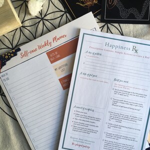 May include: A printable self-care weekly planner with a to-do list, gratitude list, and space for three things you are grateful for.  The planner is next to a printable happiness prescription with a list of simple actions to cure a bad mood.