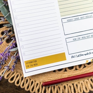 May include: A weekly planner with a checklist, space for affirmations, and prompts for reflection. The planner has a yellow and black design with the text "Hooray Corner What Brought Me Joy?", "How Can I Make Next Week Better?", and "Did I Set Time Aside To Unplug And Recharge?"