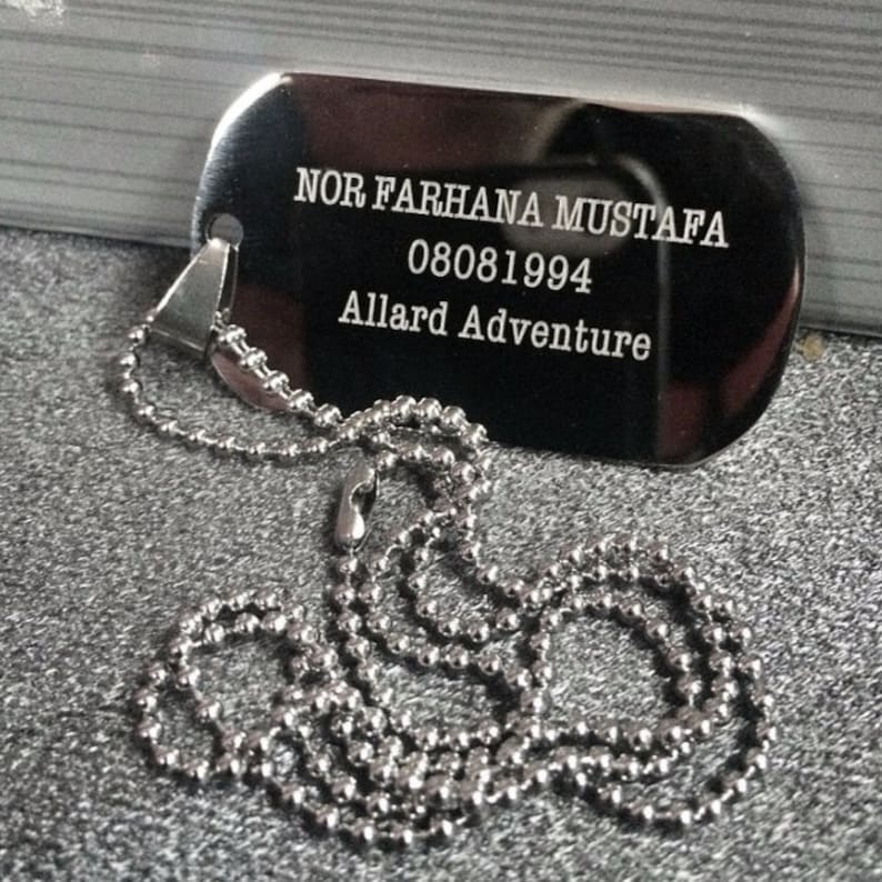 May include: Silver dog tag necklace with a ball chain. The tag is engraved with the text "NOR FARHANA MUSTAFA 08081994 Allard Adventure".