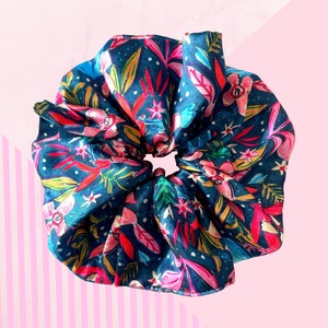 May include: A large, dark blue scrunchie with a colourful floral pattern. The design features pink, red, and green leaves and flowers, with white accents. The scrunchie is made of a silky material and is suitable for various hairstyles.
