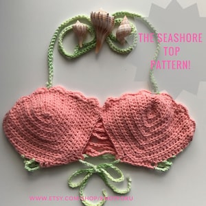 May include: A crochet top with a scalloped edge and a tie closure at the back. The top is pink and the ties are green. The text "THE SEASHORE TOP PATTERN!" is written in white on a grey starburst shape.