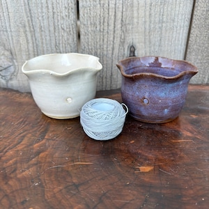 May include: Two small ceramic pots with scalloped edges, one white and one brown with blue glaze, and a ball of gray yarn.
