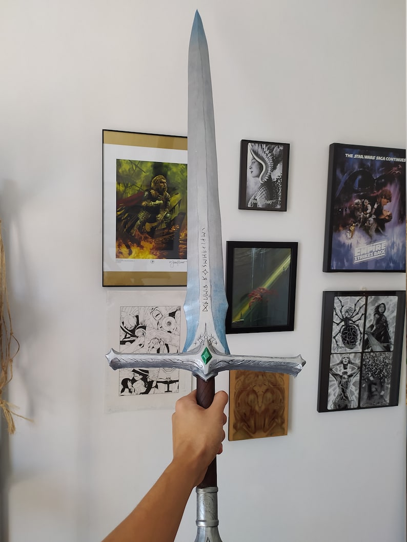 May include: A silver and blue fantasy sword with a green gem on the pommel. The blade has a silver inscription that reads "DOLGUD & SWYFT & HAF" in an ancient language.