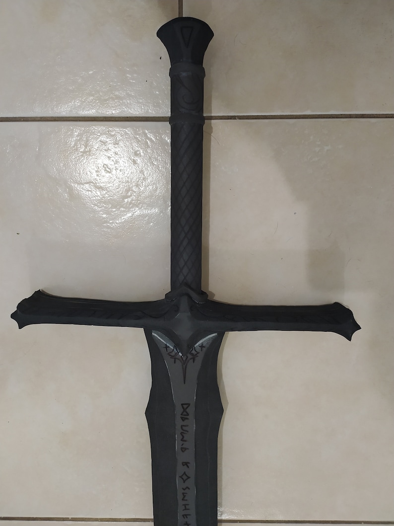 May include: A black sword with a cross guard and a black handle. The blade has a silver inscription that reads "SHIELD & SWORD" in a stylized font.