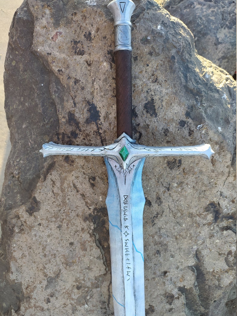 May include: A silver sword with a green gem on the pommel. The blade is decorated with a blue and white pattern and runes that read "D&Oslash;WLIG R&Oslash; SW&AElig;HF&AElig;L&AElig;".