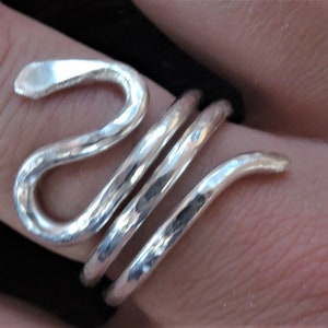 May include: A silver-colored ring in a snake design. The ring wraps around the finger with a hammered texture. The snake's head is at the top, and the body coils around the finger.