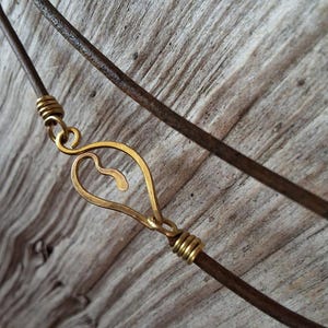 Peut inclure: Gros plan d'un collier en cordon de cuir avec un pendentif en forme de cœur en laiton. Le pendentif a un petit trou au centre.