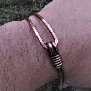 Op de afbeelding: Een koperen armband met een gehamerde afwerking en een gedraaide draadsluiting.