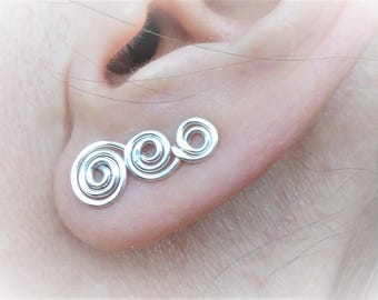 May include: Silver spiral earrings with three connected coils. The earrings are shown in a person's ear.