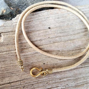 Pu&ograve; includere: Collana con cordino beige e chiusura a gancio color oro. Il cordino &egrave; intrecciato e sembra essere fatto di una fibra naturale. La chiusura e l'estremit&agrave; del cordino sono avvolte con filo color oro.