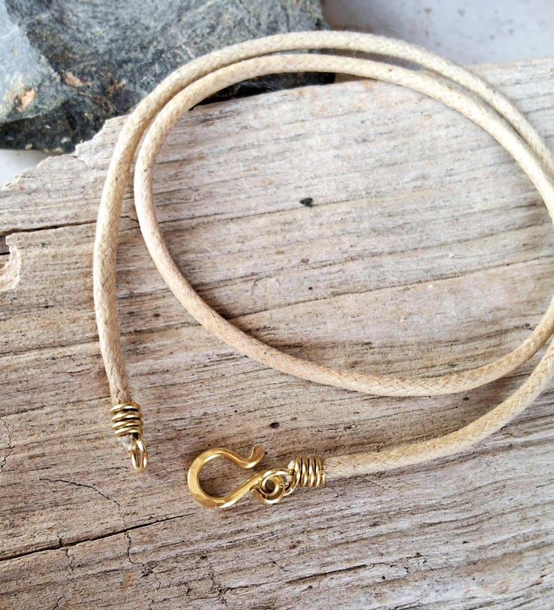 Pu&ograve; includere: Collana con cordino beige e chiusura a gancio color oro. Il cordino &egrave; intrecciato e sembra essere fatto di una fibra naturale. La chiusura e l'estremit&agrave; del cordino sono avvolte con filo color oro.