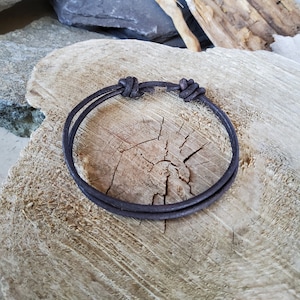 Pode incluir: Um bracelete de couro castanho escuro com um design de nó simples.