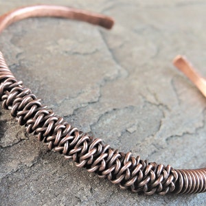 May include: A copper bracelet featuring a woven design. The bracelet is crafted from a single piece of copper wire, intricately woven to create a distinctive pattern.