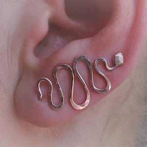 Op de afbeelding: Een paar rose gouden slang oormanchetten. De manchetten zijn gemaakt van gehamerd metaal en zijn gevormd als een slang. De manchetten worden op het bovenste deel van het oor gedragen.