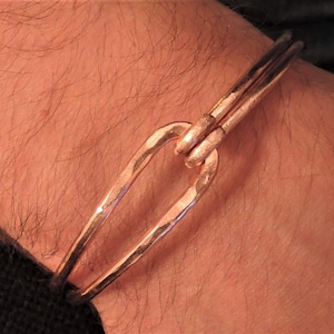 May include: A copper bangle bracelet with a unique, hammered finish and a simple, open-loop design.