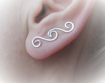 May include: Silver ear cuff with a delicate, wave-like design. The cuff is made of thin, twisted wire and is designed to be worn on the upper ear.