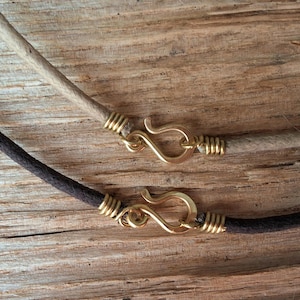 Pu&ograve; includere: Primo piano di due collane con fili simili a corde. Una &egrave; color beige chiaro, l'altra marrone scuro. Entrambe hanno chiusure a gancio color oro e avvolgimento di filo alle estremit&agrave;. Lo sfondo &egrave; una superficie di legno strutturata.