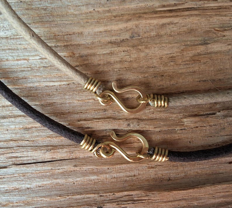 Pu&ograve; includere: Primo piano di due collane con fili simili a corde. Una &egrave; color beige chiaro, l'altra marrone scuro. Entrambe hanno chiusure a gancio color oro e avvolgimento di filo alle estremit&agrave;. Lo sfondo &egrave; una superficie di legno strutturata.