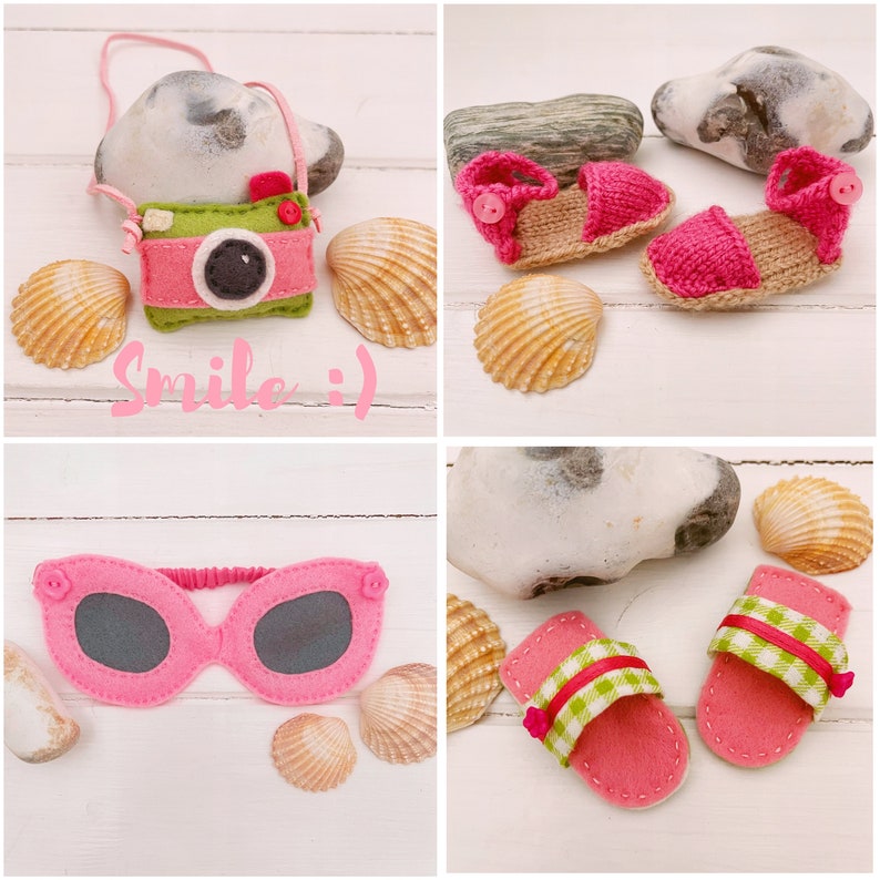 May include: A set of felt crafts featuring a pink camera with the text "Smile :)", pink sunglasses, and pink and green sandals. The crafts are arranged on a white wooden background with seashells.