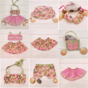 May include: A set of doll clothes in pink and green with floral patterns. The set includes a skirt, a top, a hat, shorts, and a bag. The clothes are made of fabric and have a variety of textures.