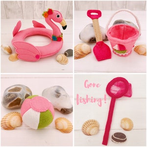 May include: A pink felt flamingo pool float, a pink felt bucket with a white sailboat design, a pink felt shovel, a pink felt beach ball with white and green panels, and a pink felt fishing net with a red handle. The text "Gone fishing!" is written in pink on a white background.