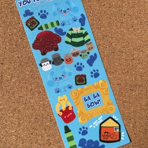 May include: A blue sticker sheet featuring various cartoon images, including a red armchair, a green and white striped sweater, and paw prints. Text includes "YOU FOUND A CLUE!" and "BA BA BOW!"