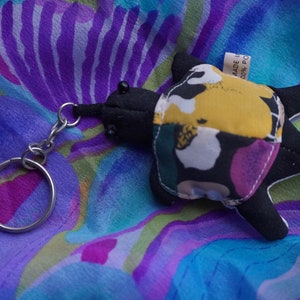 May include: A black and yellow patchwork turtle keychain with a silver key ring. The turtle is made of fabric and has a tag that says "MADE IN CHINA 100% POLYESTER".