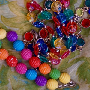 K&ouml;nnte beinhalten: Eine bunte Perlenkette mit verschiedenen Formen und Gr&ouml;&szlig;en. Die Perlen sind aus Glas und Kunststoff und auf einer silbernen Kette aufgef&auml;delt. Die Kette ist ein lebendiger Mix aus Rot, Gelb, Blau, Gr&uuml;n und Lila.