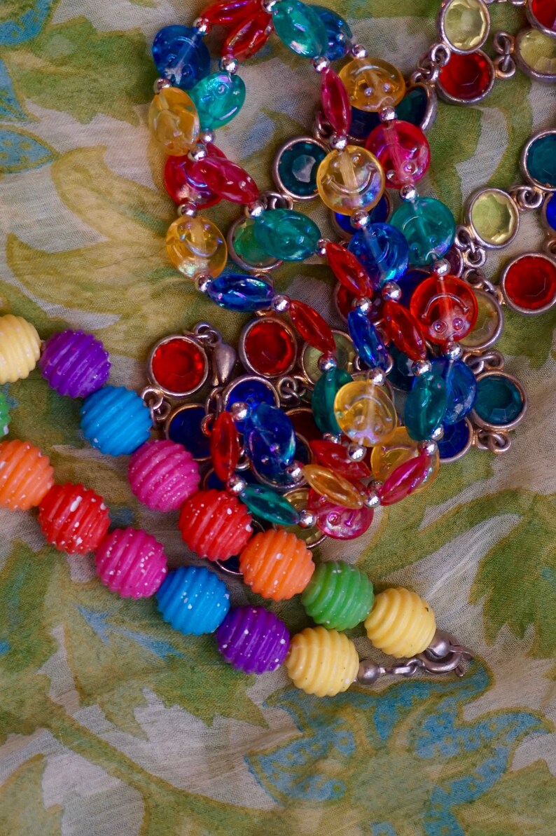 K&ouml;nnte beinhalten: Eine bunte Perlenkette mit verschiedenen Formen und Gr&ouml;&szlig;en. Die Perlen sind aus Glas und Kunststoff und auf einer silbernen Kette aufgef&auml;delt. Die Kette ist ein lebendiger Mix aus Rot, Gelb, Blau, Gr&uuml;n und Lila.