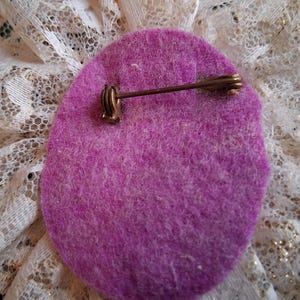 Puede incluir: La parte posterior de un broche de flor de fieltro morado con un alfiler de metal dorado.