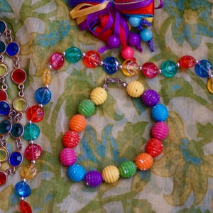 K&ouml;nnte beinhalten: Eine bunte Perlenkette und ein Armband mit regenbogenfarbenen Perlen. Die Kette und das Armband bestehen aus Plastikperlen mit einer strukturierten Oberfl&auml;che. Die Perlen sind auf einem silbernen Draht aufgef&auml;delt.