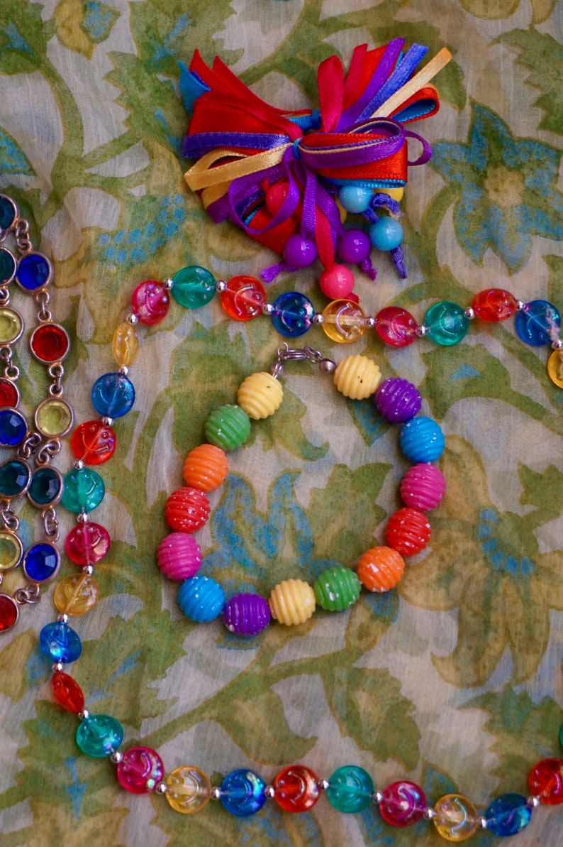 K&ouml;nnte beinhalten: Eine bunte Perlenkette und ein Armband mit regenbogenfarbenen Perlen. Die Kette und das Armband bestehen aus Plastikperlen mit einer strukturierten Oberfl&auml;che. Die Perlen sind auf einem silbernen Draht aufgef&auml;delt.