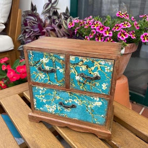 May include: A wooden box with three drawers featuring a blue and white floral print. The drawers have antique-style metal handles.
