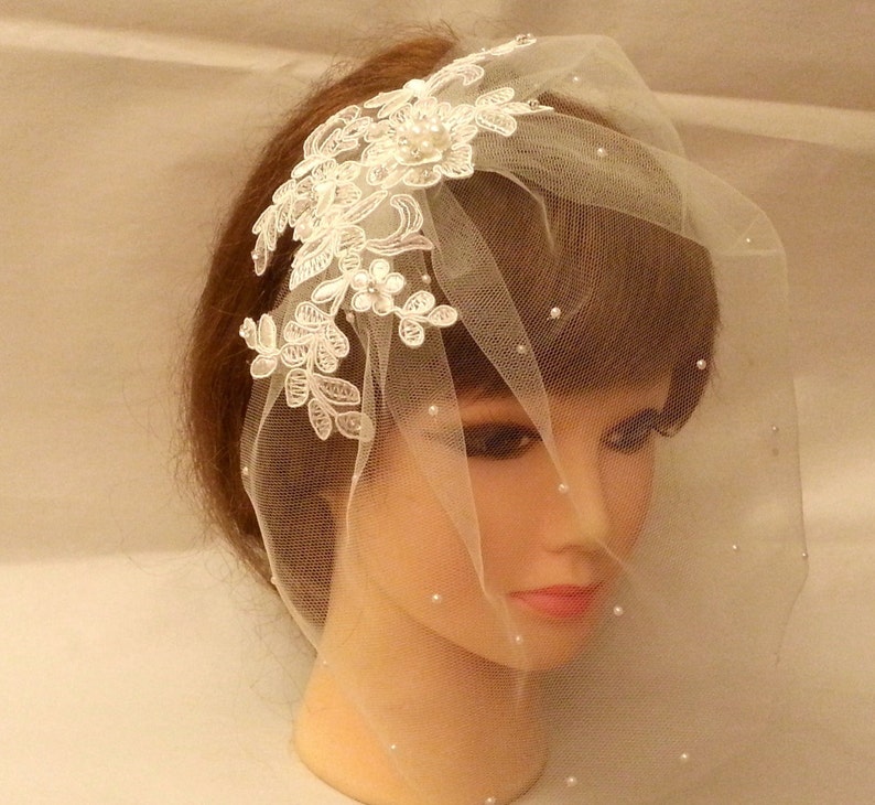 May include: A white bridal veil with a delicate lace design and pearl embellishments. The veil is made of soft tulle and is perfect for a wedding or special occasion.