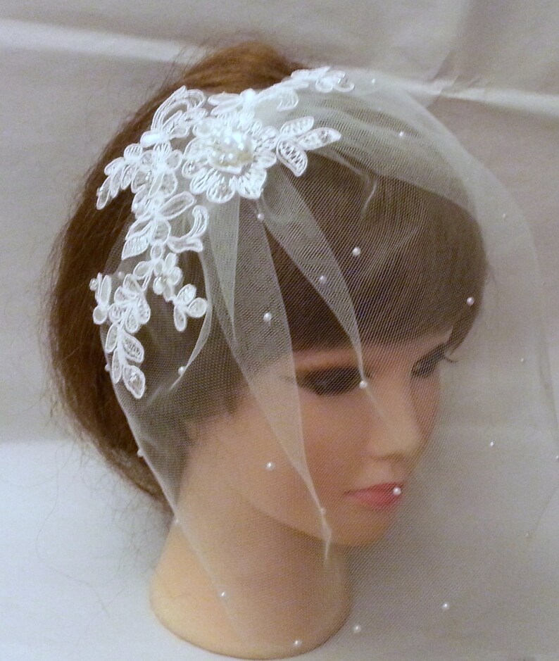 May include: White bridal veil with a delicate lace applique and pearl embellishments. The veil is made of soft tulle and is perfect for a simple and elegant wedding look.