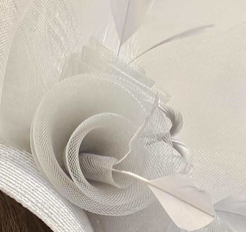May include: White feather and tulle flower hat with a delicate, layered design. The hat is made of soft, white tulle and features a single white feather.