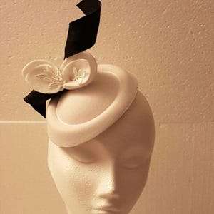 Peut inclure: Un chapeau en feutre blanc avec un ruban noir et une fleur blanche.