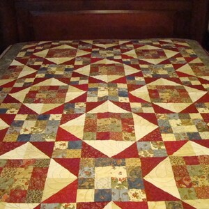 May include: A patchwork quilt with a geometric pattern in shades of red, cream, and green. The quilt is made of various fabrics with floral and geometric designs.