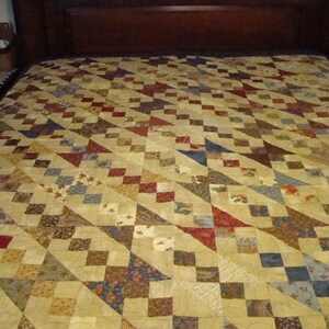May include: A quilt with a geometric pattern featuring a variety of fabrics in shades of brown, red, blue, and cream.