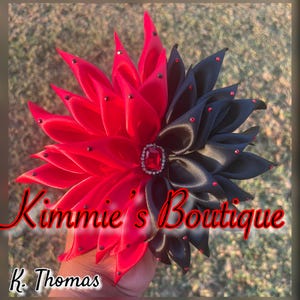 May include: A two-toned floral hair accessory, half red and half black, adorned with red rhinestones. The center features a large, rectangular red jewel. The text "Kimmie's Boutique" and "K. Thomas" are visible.