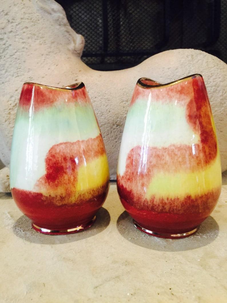 May include: Two colorful, egg-shaped vases with a red base, a yellow and white midsection, and a green top. The vases have a gold rim and a glossy finish. The background is a neutral color.