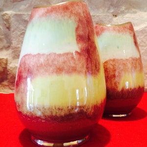 May include: Two decorative glass vases with a layered color scheme. The vases have a bulbous shape with a narrow neck and a silver-colored base. The color scheme includes shades of red, yellow, and green, creating a unique and artistic appearance.