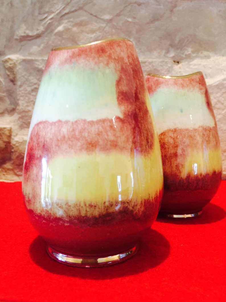 May include: Two decorative glass vases with a layered color scheme. The vases have a bulbous shape with a narrow neck and a silver-colored base. The color scheme includes shades of red, yellow, and green, creating a unique and artistic appearance.