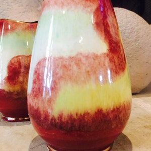 May include: A pair of decorative vases with a teardrop shape. The vases feature a vibrant color palette of red, yellow, and white, with a glossy finish. The base of each vase has a silver rim.
