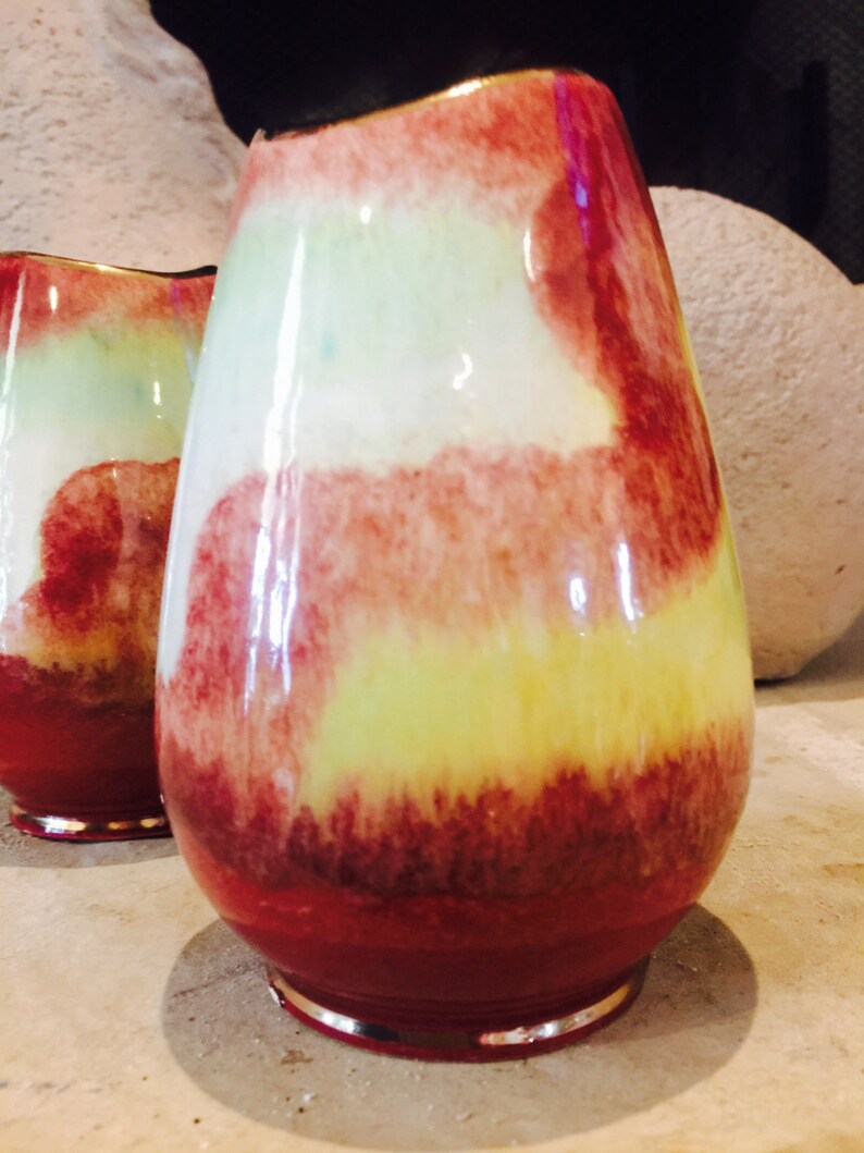 May include: A pair of decorative vases with a teardrop shape. The vases feature a vibrant color palette of red, yellow, and white, with a glossy finish. The base of each vase has a silver rim.