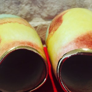 May include: Two ceramic vases with a yellow, red, and green color scheme. The vases have a gold rim and a dark interior. The vases are set against a neutral background and a red surface.